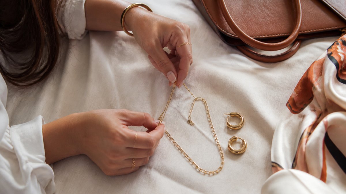 Woman arranging gold necklace and hoop earrings on linen, ideal as best gift ideas for stylish women